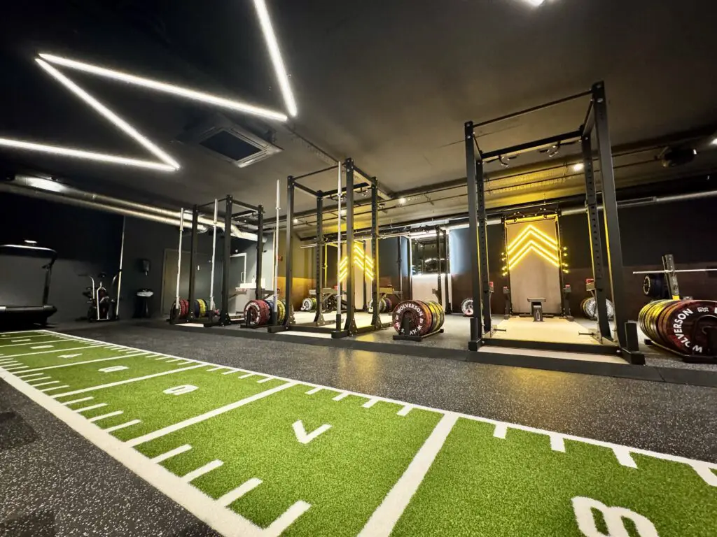 A photograph of the inside of Jetts Farnham, including a weight sliding track running from left to right, in front of a row of olympic weightlifting stations.