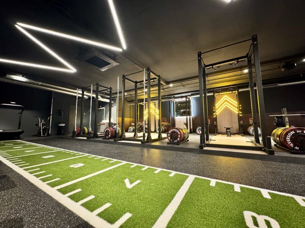 A photograph of the inside of Jetts Farnham, including a weight sliding track running from left to right, in front of a row of olympic weightlifting stations.