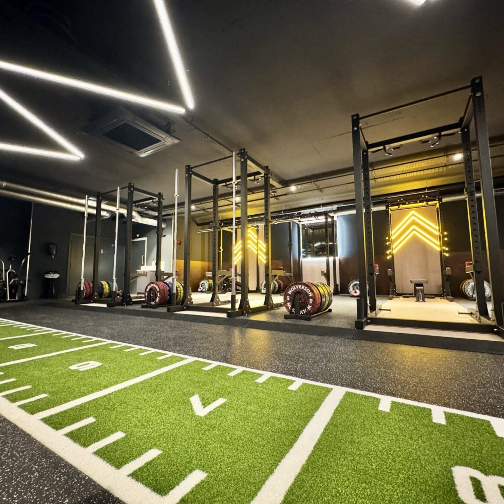 A photograph of the inside of Jetts Farnham, including a weight sliding track running from left to right, in front of a row of olympic weightlifting stations.